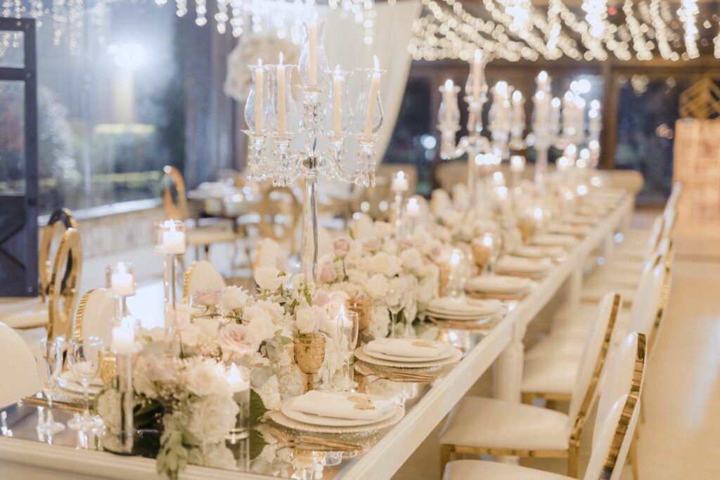 Centro de mesa de boda con candelabros de cristal, flores blancas y rosas, velas encendidas y detalles dorados, decoración elegante y romántica para recepción nupcial