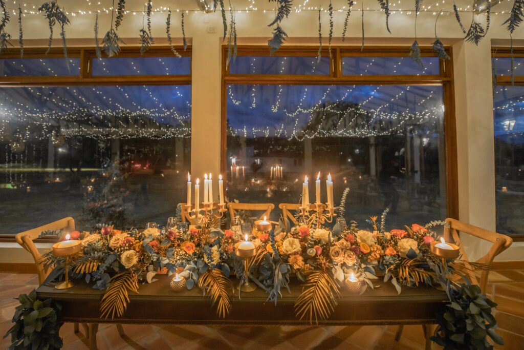 Centro de mesa elegante con velas doradas y flores modernas, 33 centros de mesa para bodas modernos y espectaculares que te robarán suspiros, Decoración romántica con candelabros y flores en tonos cálidos para bodas, Mesa de boda iluminada con velas y centros florales sofisticados, Centros de mesa modernos con velas y follaje dorado en decoración nupcial, Arreglo floral nocturno con velas y detalles metálicos para boda elegante, Decoración de recepción con centros de mesa espectaculares y románticos, Centros de mesa para bodas con velas altas y flores en tendencia, Diseño de mesa nupcial con iluminación cálida y flores modernas, Arreglo floral minimalista y sofisticado con velas para boda nocturna, Centros de mesa modernos y espectaculares con velas románticas