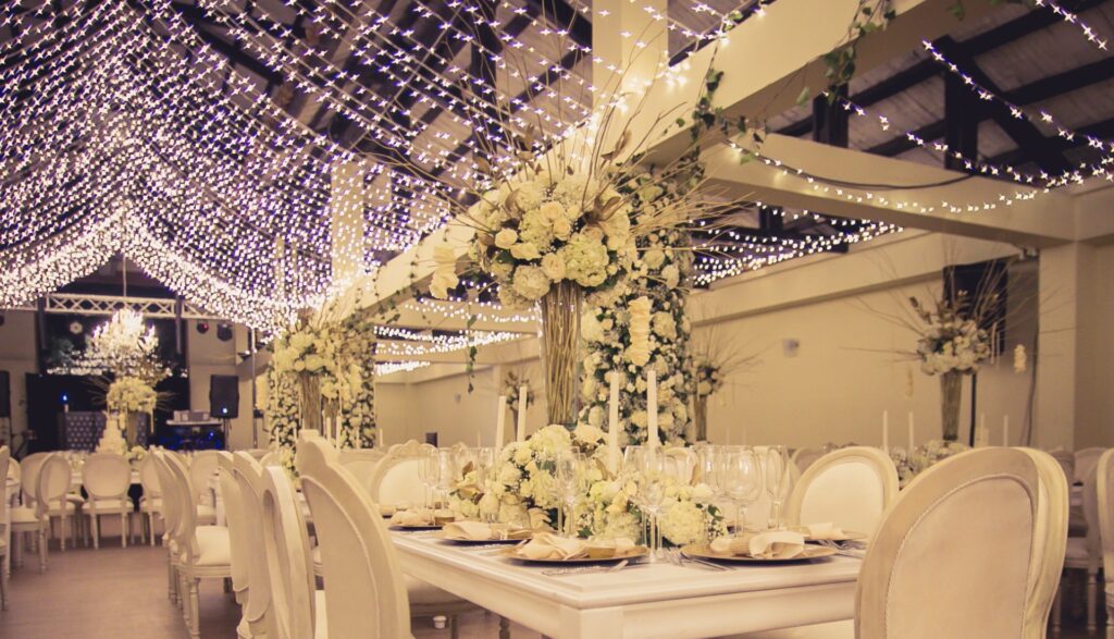 Centro de mesa elegante para boda con rosas y hortensias blancas, ramas doradas en copa de cristal y decoración con techo de luces tipo cielo estrellado