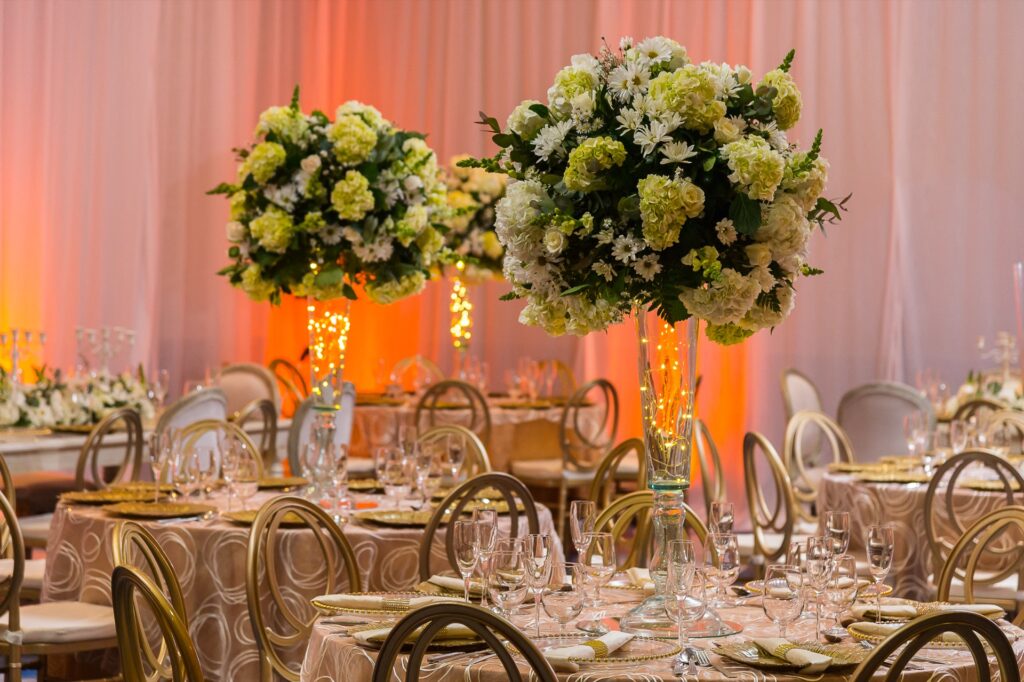Centro de mesa alto con hortensias y luces cálidas en boda elegante con decoración dorada y manteles neutros.