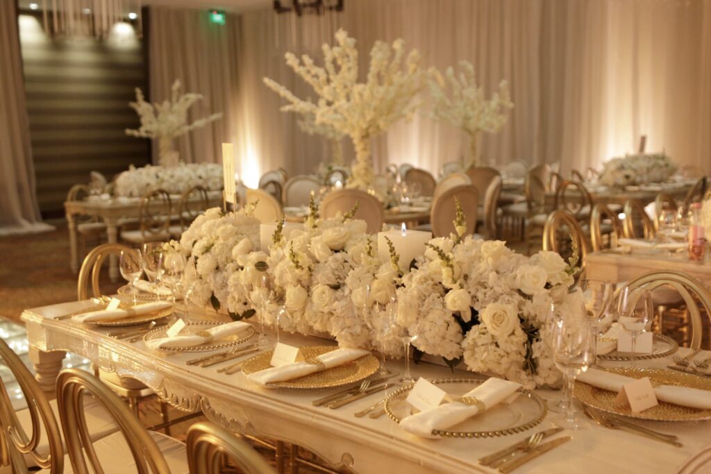 Centro de mesa de boda elegante con guirnalda de flores blancas, velas románticas y vajilla dorada sobre mesa rectangular