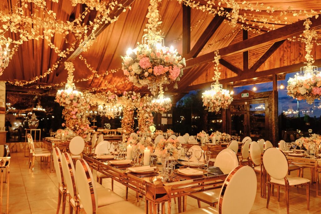 Decoración de boda elegante con techos iluminados por guirnaldas de luces cálidas, centros de mesa florales y candelabros colgantes decorados con flores en tonos pastel